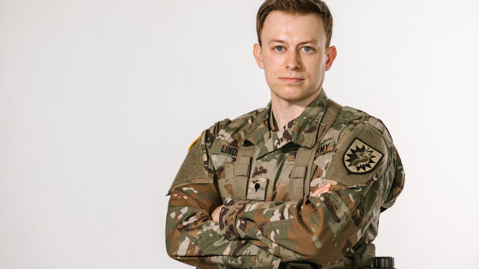 A U.S. Army soldier in camouflage uniform standing with arms crossed.