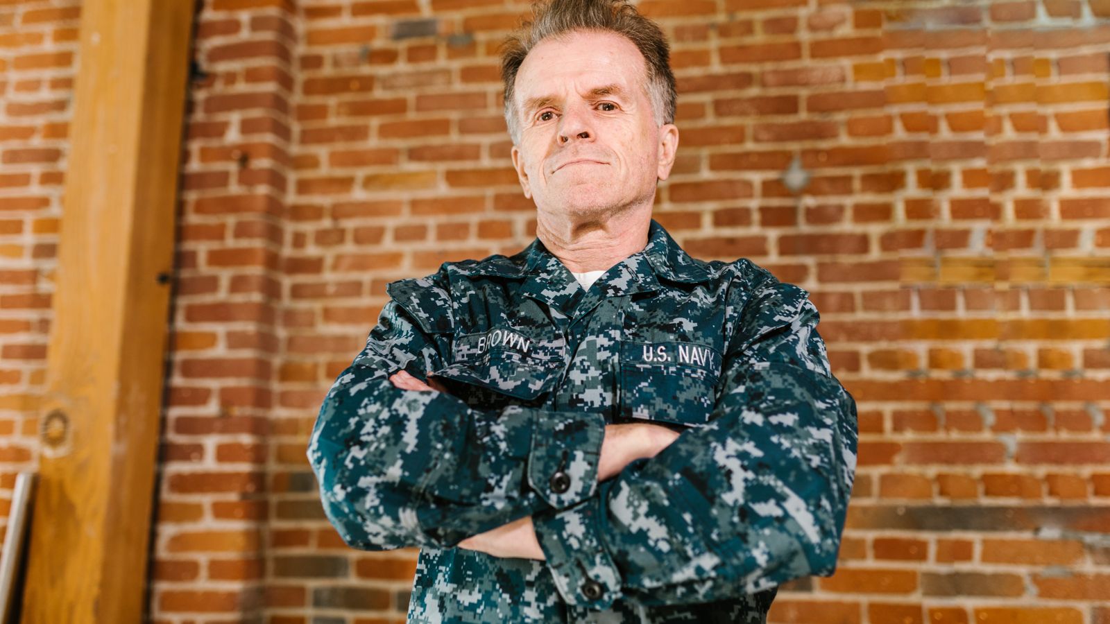 Proud US Navy veteran standing confidently in military uniform with brick background.
