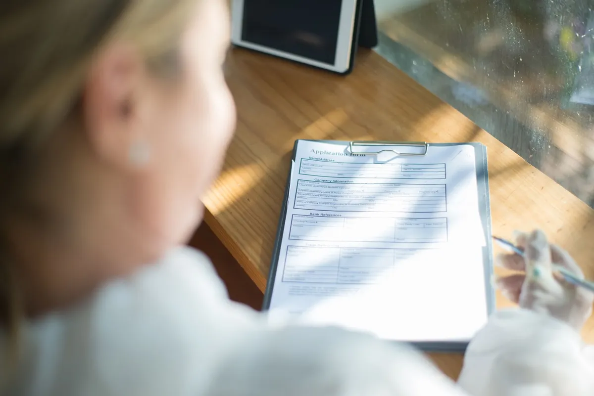 Hands filling out a paper benefits application form on a clipboard