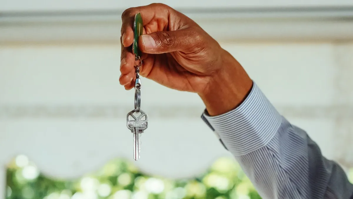 A hand holding a single house key on a keyring