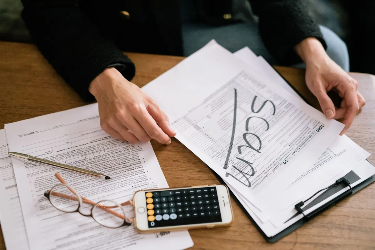 Tax forms, a calculator and a pen laid out on a wooden kitchen table