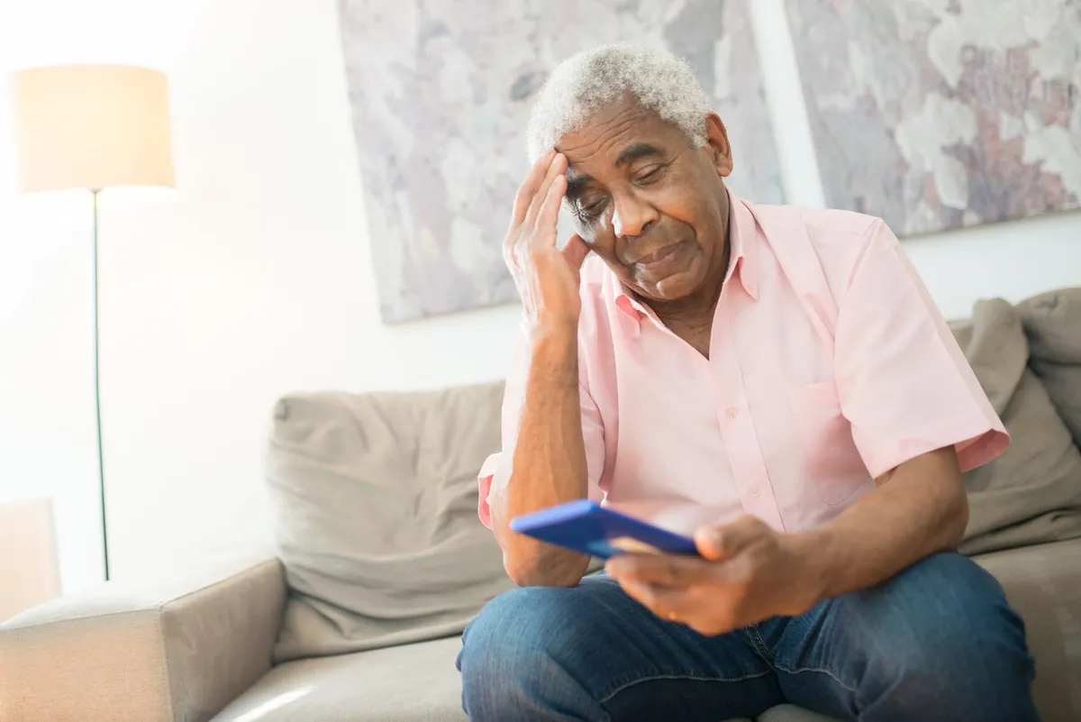 An older man looking at his phone with a worried expression