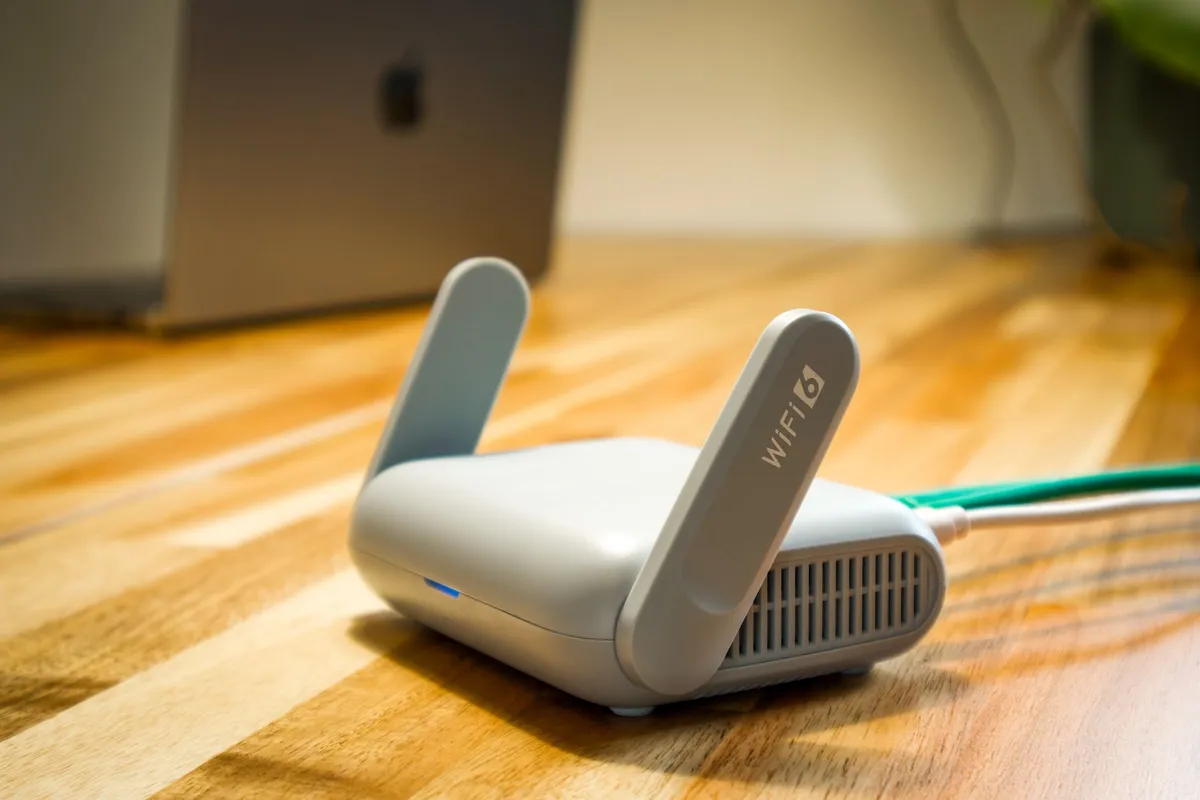 A smartphone lying face up on a wooden table next to a Wi-Fi router