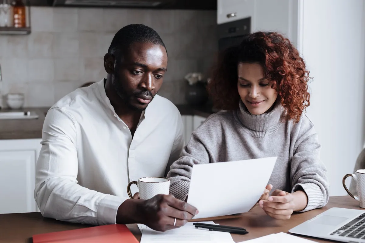 Two roommates sitting in a shared apartment kitchen looking at paperwork together